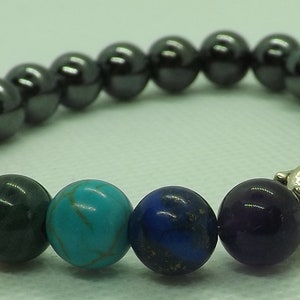 May include: A beaded bracelet with a silver Buddha charm. The bracelet features seven chakra stones in the colors of red, orange, yellow, green, blue, indigo, and violet. The bracelet is made with black hematite beads.