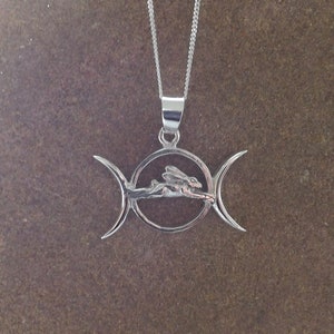 May include: Silver pendant necklace featuring a triple moon symbol with a stylized hare or rabbit inside the circle.