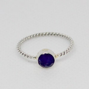 May include: A silver ring with a twisted band and a dark purple gemstone.