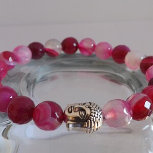 May include: A pink and white agate gemstone bracelet with a silver Buddha head charm.