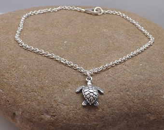 May include: A silver chain anklet with a small silver turtle charm. The anklet is on a brown rock.