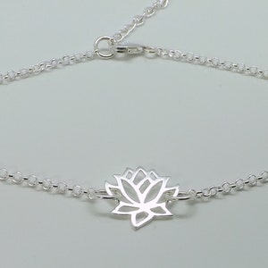 Puede incluir: Un brazalete de cadena de plata con un delicado dije de flor de loto. La cadena es de estilo simple y enlazada.