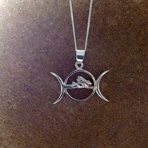 May include: A silver pendant necklace featuring a triple moon symbol with a stylized rabbit running through the center circle.