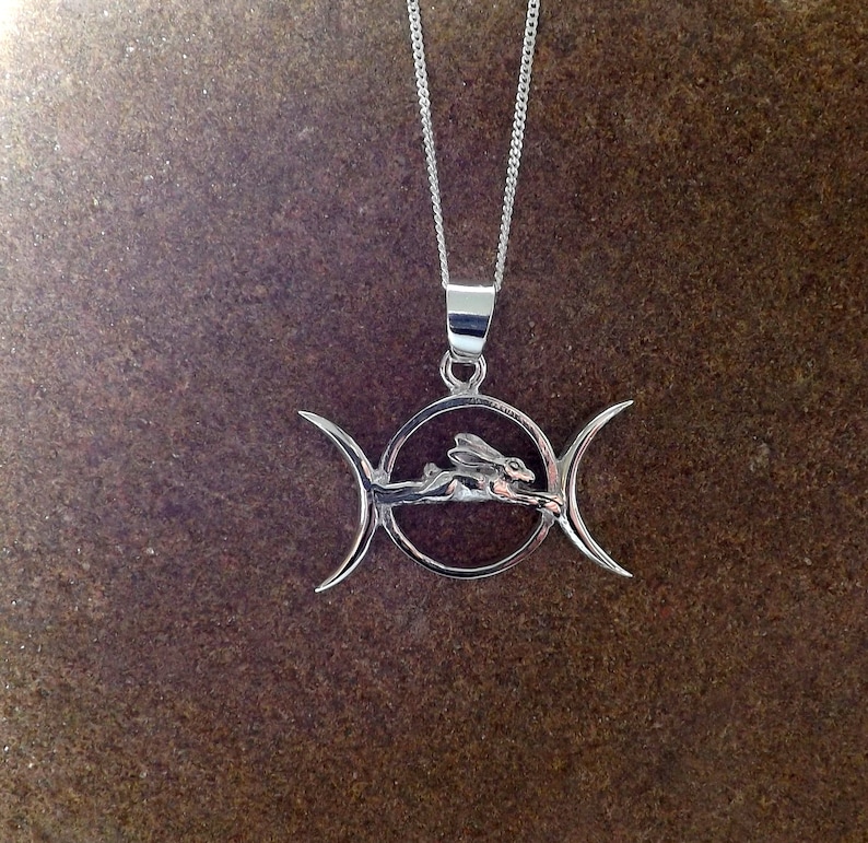 May include: A silver pendant necklace featuring a triple moon symbol with a stylized rabbit running through the center circle.