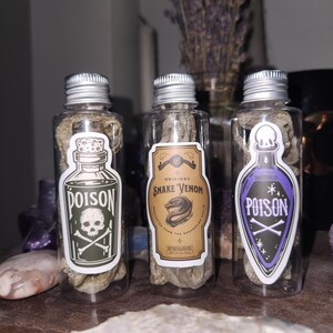 May include: Three clear glass bottles with silver lids, each containing a dried, textured material. The bottles have labels that read "Poison" with a skull and crossbones, and "Snake Venom". The labels are in various colours.