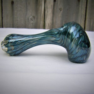 May include: A teal glass pipe with gold swirls. The pipe is shaped like a traditional pipe with a bowl and a stem.
