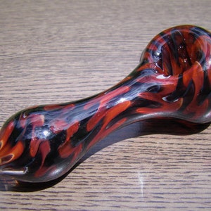 May include: A red and black glass pipe with a swirl pattern. The pipe is made of glass and has a bowl on one end and a mouthpiece on the other.