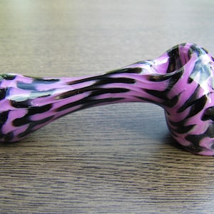 May include: A pink and black glass pipe with a swirl pattern. The pipe is made of glass and has a bowl on one end and a mouthpiece on the other.