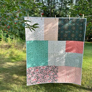 May include: A patchwork quilt featuring a variety of fabric squares in shades of peach, teal, dark green, and white. The quilt displays diverse patterns including floral prints, small geometric shapes, and solid colors, all finished with white binding.