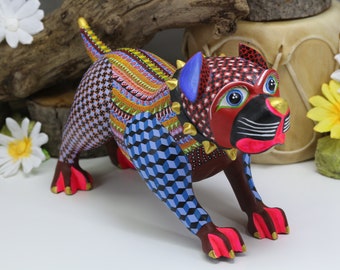 May include: A colorful wooden carved dog figurine with a red, black, and white face, blue and white patterned body, and gold accents. The dog is standing on all fours with its head tilted to the side.