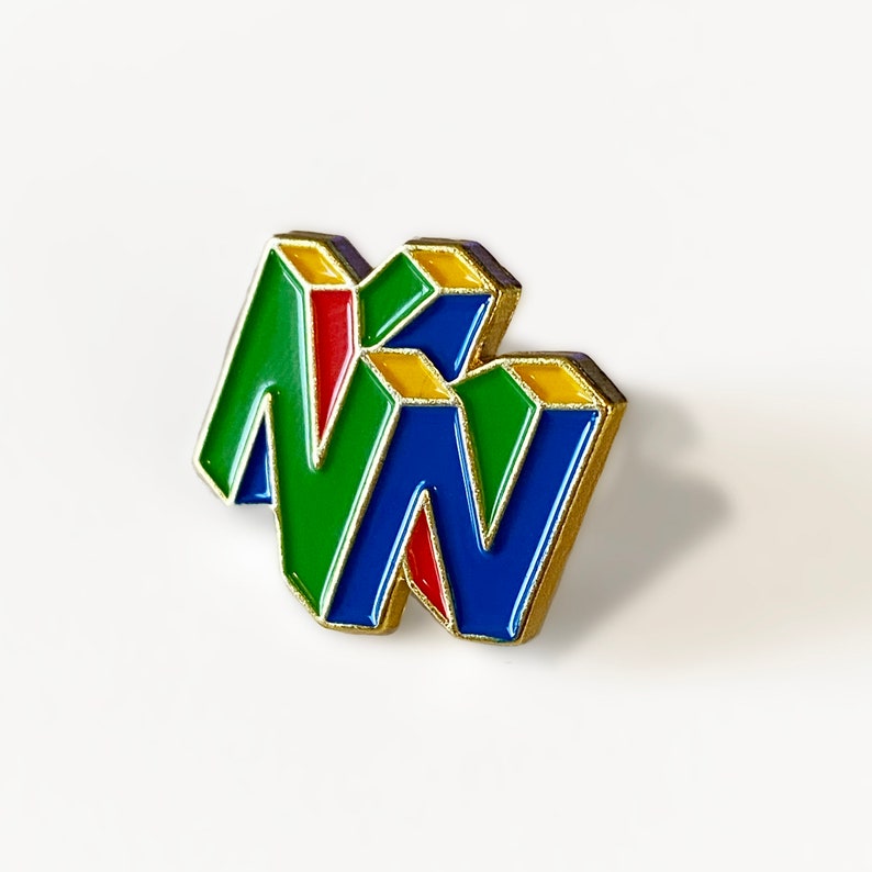 Peut inclure: Une &eacute;pingle &eacute;maill&eacute;e color&eacute;e repr&eacute;sentant le logo "N64" en vert, bleu et rouge, avec des bordures dor&eacute;es. Cette &eacute;pingle est un objet de collection pour les fans de jeux vid&eacute;o r&eacute;tro.