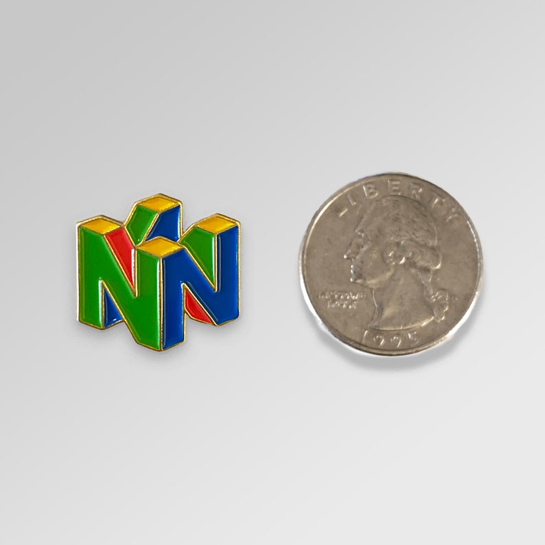 Peut inclure: Une &eacute;pingle &eacute;maill&eacute;e color&eacute;e repr&eacute;sentant le logo Nintendo 64 en vert, rouge, bleu et jaune. L'&eacute;pingle est &agrave; c&ocirc;t&eacute; d'une pi&egrave;ce de monnaie am&eacute;ricaine pour comparaison de taille. L'&eacute;pingle a une bordure dor&eacute;e.