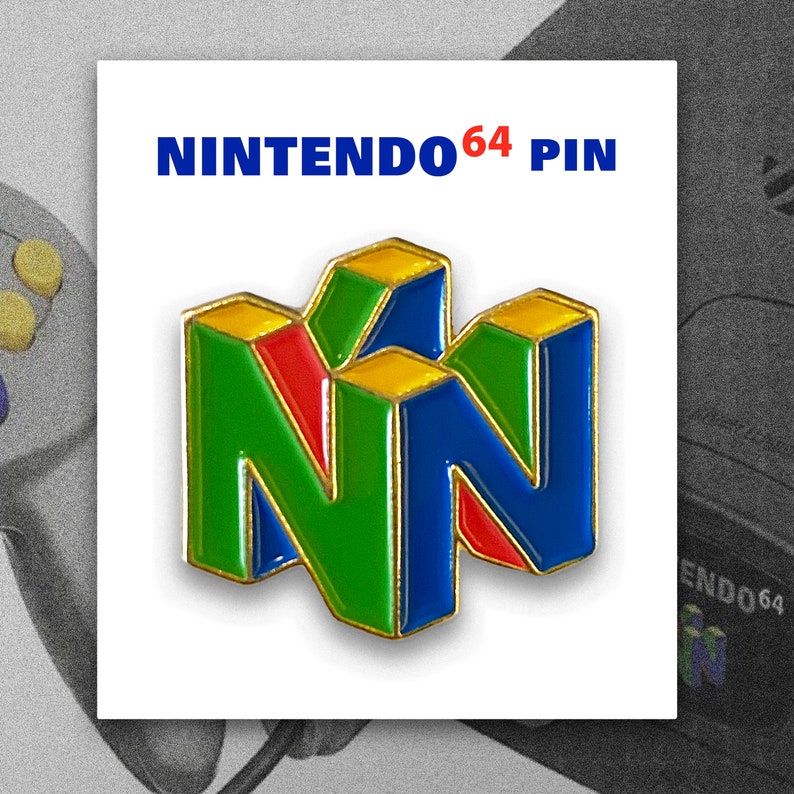 Peut inclure: &Eacute;pinglette Nintendo 64 color&eacute;e avec le logo embl&eacute;matique vert, rouge et bleu, bord&eacute;e d'or. Le texte "NINTENDO 64 PIN" en bleu et rouge est affich&eacute; sur un fond blanc.