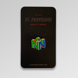 Peut inclure: Une &eacute;pingle &eacute;maill&eacute;e color&eacute;e repr&eacute;sentant le logo Nintendo 64 en vert, rouge et bleu. L'&eacute;pingle est pr&eacute;sent&eacute;e sur une carte noire avec le texte "ST. PROVISIONS QUALITY GOODS" et "SAINTPROVISIONS.COM". Un objet de collection.