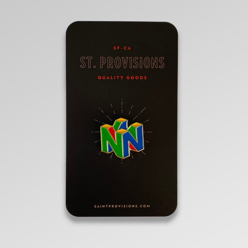 Peut inclure: Une &eacute;pingle &eacute;maill&eacute;e color&eacute;e repr&eacute;sentant le logo Nintendo 64 en vert, rouge et bleu. L'&eacute;pingle est pr&eacute;sent&eacute;e sur une carte noire avec le texte "ST. PROVISIONS QUALITY GOODS" et "SAINTPROVISIONS.COM". Un objet de collection.