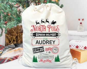May include: A white canvas Santa sack with a red and black design. The sack has the text "North Pole Express Delivery for Audrey" and a stamp that says "Do Not Open Until December 25".