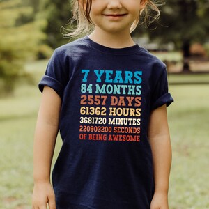 May include: A navy blue t-shirt with a colorful graphic that reads "7 Years, 84 Months, 2557 Days, 61362 Hours, 3681720 Minutes, 220903200 Seconds of Being Awesome".