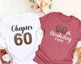 May include: Two t-shirts with a leopard print design. The white t-shirt says "Chapter 60" and the coral pink t-shirt says "60th Birthday Crew".
