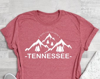 May include: Coral pink t-shirt with a white graphic of mountains and trees. The text "Never Stop Exploring" and "Tennessee" are printed on the shirt.