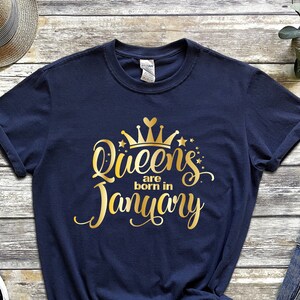 May include: Navy blue t-shirt with gold lettering that reads "Queens are born in January" and a gold crown graphic.