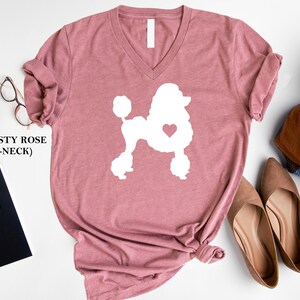 Puede incluir: Camiseta de cuello en V rosa polvoriento con una silueta blanca de un caniche con un coraz&oacute;n en el pecho.
