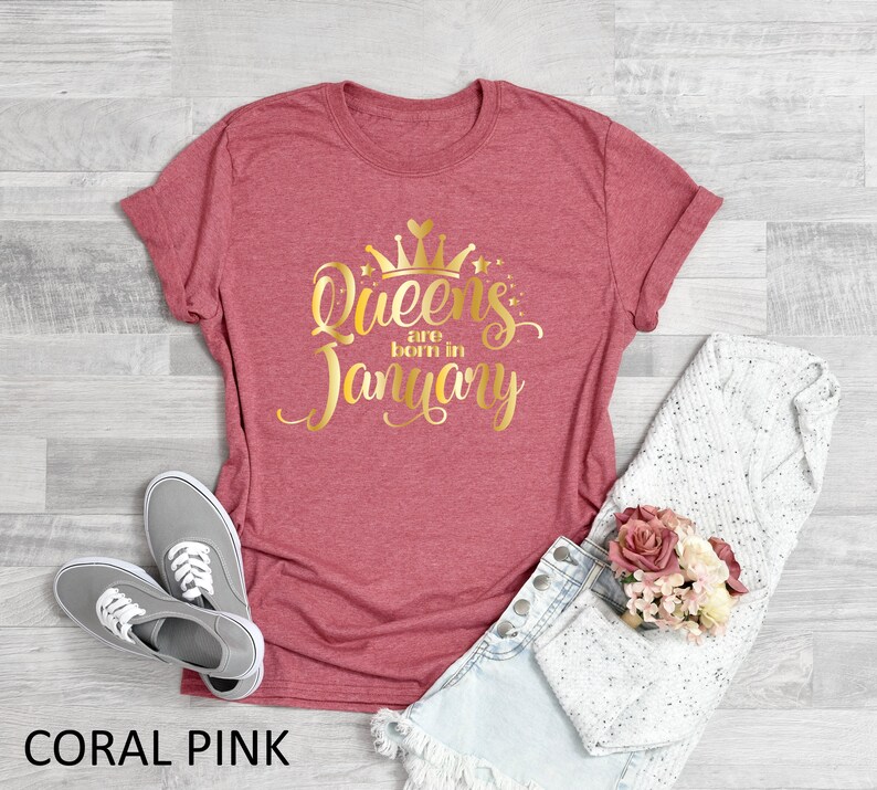 May include: Coral pink t-shirt with gold glitter text that reads "Queens are born in January" and a gold glitter crown above the text.