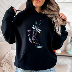 May include: Black hooded sweatshirt with a colorful dragonfly design. The dragonfly is surrounded by feathers and has a watercolor effect.