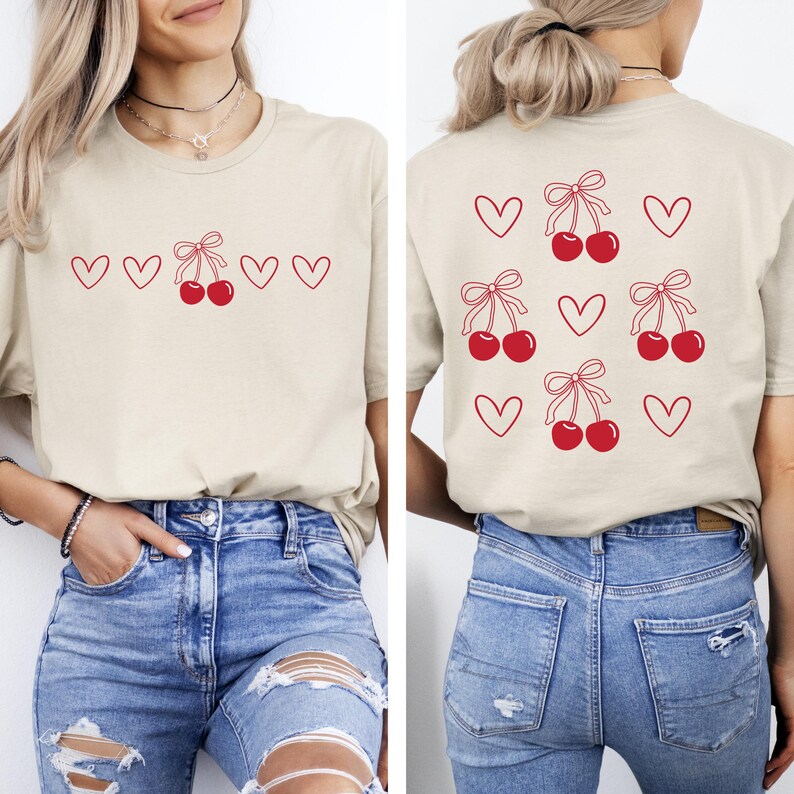 May include: A beige t-shirt with a red cherry and heart design on the front and back. The front design has five hearts and a cherry with a bow. The back design has six hearts and three cherries with bows.
