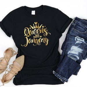 May include: Black t-shirt with gold lettering that says "Queens are born in January" with a gold crown above the text.