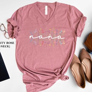May include: Dusty rose V-neck t-shirt with the word "nana" in white script surrounded by colourful floral embroidery.