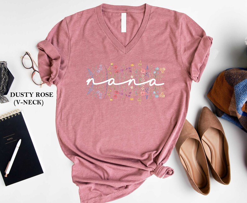 May include: Dusty rose V-neck t-shirt with the word "nana" in white script surrounded by colourful floral embroidery.