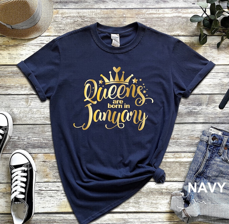 May include: Navy blue t-shirt with gold lettering that reads "Queens are born in January" and a gold crown graphic.