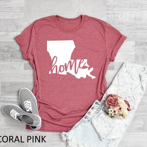 May include: Coral pink t-shirt with a white outline of the state of Louisiana and the word "home" written inside the state.