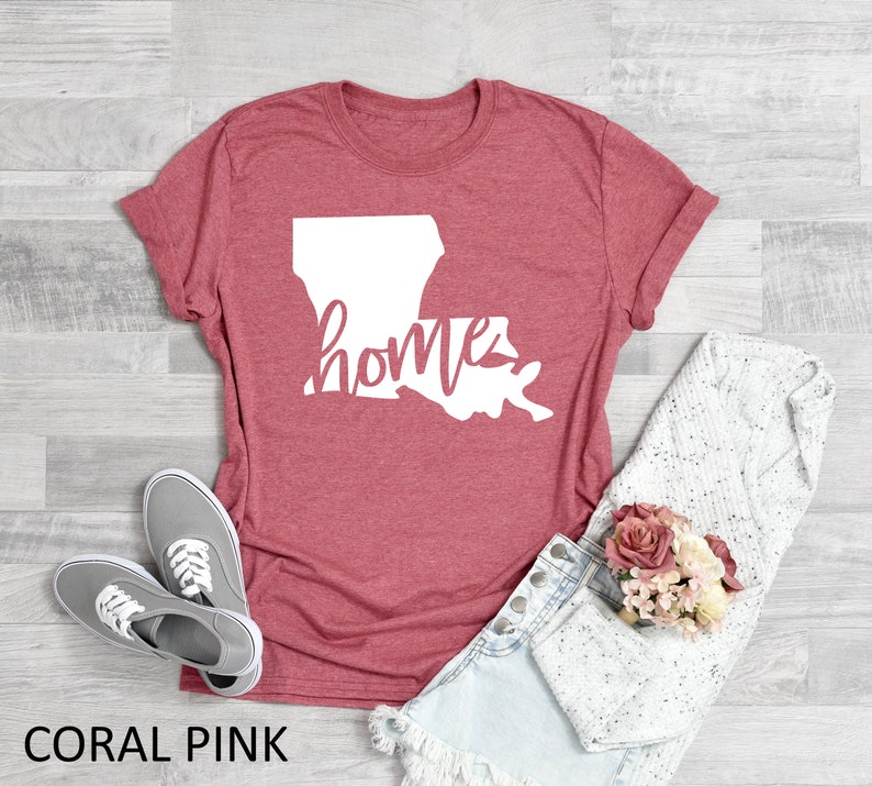 May include: Coral pink t-shirt with a white outline of the state of Louisiana and the word "home" written inside the state.