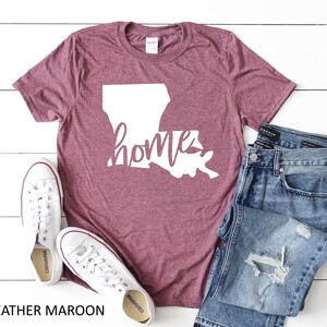 May include: Heather maroon t-shirt with a white outline of the state of Louisiana and the word "home" written in a white cursive font.