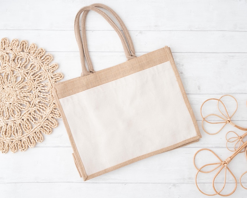 May include: A beige tote bag with a white fabric insert. The bag has a natural woven texture and is made of burlap. The bag is lying flat on a white wooden surface.
