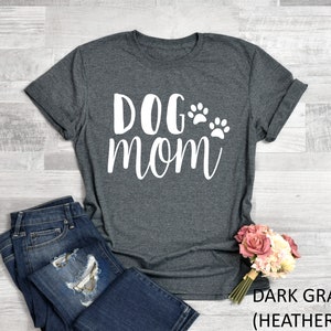 May include: Dark gray heather t-shirt with the words "DOG mom" in white script, accompanied by two paw prints. The shirt is paired with blue jeans and a bouquet of pink and white flowers.