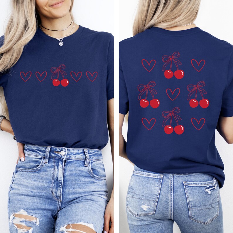 May include: A navy blue t-shirt with a red cherry and bow design on the front and back. The design features multiple cherries with bows and hearts.