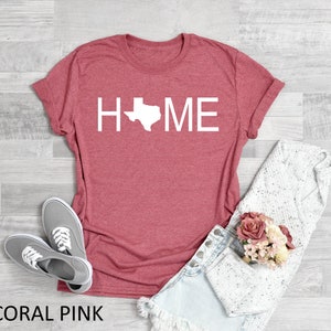 May include: Coral pink t-shirt with the word "HOME" in white text with the outline of the state of Texas replacing the "O".
