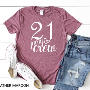 May include: Heather maroon t-shirt with the text "21 party crew" in white. The shirt is paired with blue jeans and white sneakers. The image also includes the text "HEATHER MAROON".