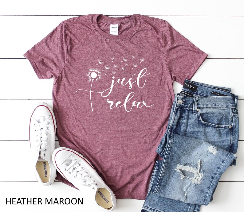May include: Heather maroon t-shirt with a white dandelion graphic and the text "just relax". The shirt is laid flat on a white surface with a pair of white sneakers and blue jeans.