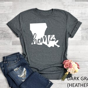 May include: Dark gray heather t-shirt with a white outline of the state of Louisiana and the word "home" written inside the state.