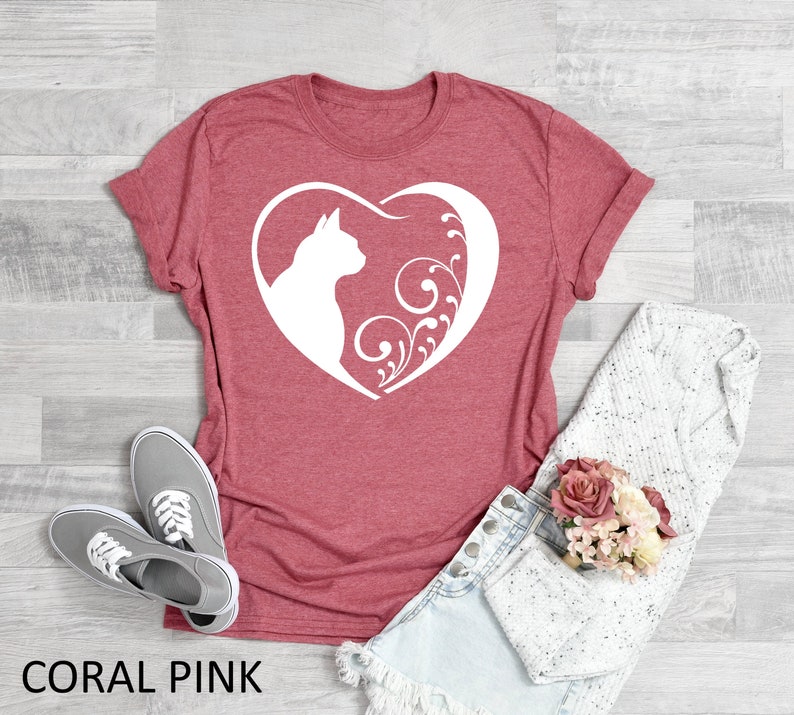 May include: Coral pink t-shirt with a white silhouette of a cat inside a heart with floral designs.