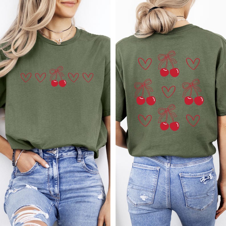 May include: A green t-shirt with a cherry and heart design on the front and back. The front design has a row of cherries with bows and hearts. The back design has multiple cherries with bows and hearts.