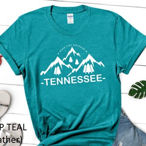 May include: Teal heather t-shirt with a white graphic of mountains and trees. The graphic says "Never Stop Exploring - Tennessee - "