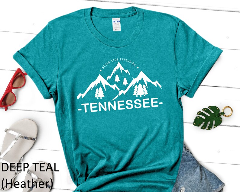 May include: Teal heather t-shirt with a white graphic of mountains and trees. The graphic says "Never Stop Exploring - Tennessee - "