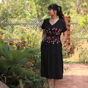 May include: A black midi dress with short sleeves and a V-neckline. The dress features pink floral embroidery around the waist.