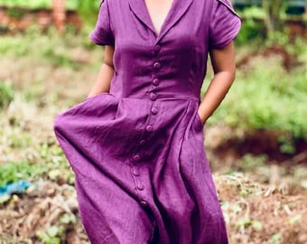 May include: A purple linen dress with a collared neckline and button closure. The dress has short sleeves and a flowing skirt.