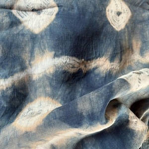 Puede incluir: Primer plano de una tela azul y blanca teñida anudada con una textura arrugada. La tela tiene un fondo azul claro con patrones de teñido anudado blancos y tostados.