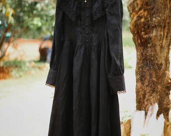 May include: A black long-sleeved dress with a lace collar and a button-up front. The dress has a ruffled hem and is hanging on a wooden hanger.